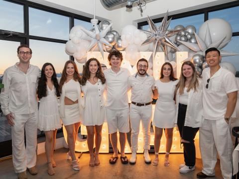 Alumni dressed in white stand in front of ballons at a party