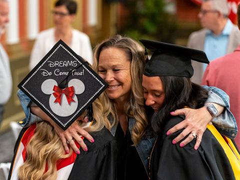 Woman hugging two young women in graduate caps and gowns