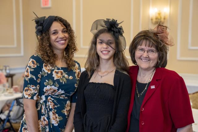 Three women smiling, dressed in hats for a formal tea