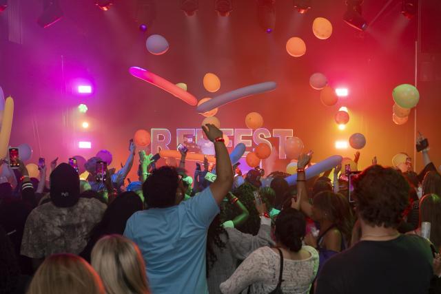 People partying in front of a stage with balloons and lights